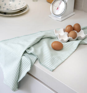 Bruine eieren in een witte keramische schaal, met één ei op de Walra-theedoek Superior Dry Cloth Jade naast een weegschaal en een stapel borden.