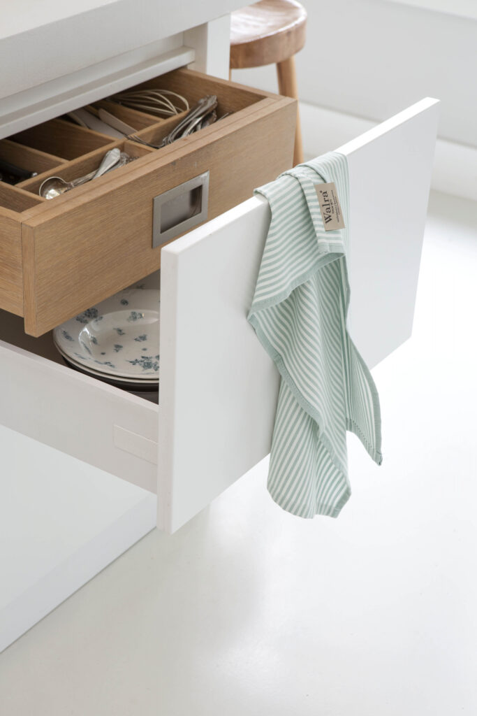 Een open keukenlade met daarin een houten bestekbak en borden, met de Walra Theedoek Superior Dry Cloth Jade eroverheen gedrapeerd.