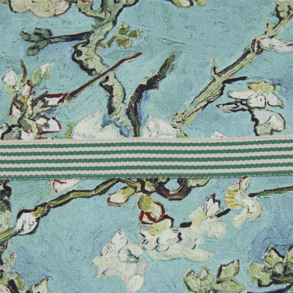 Deze close-up toont het VanGogh Blossom-schort in blauw met witte bloesemtakken op een lichtblauwe achtergrond en een groen-wit gestreept lint in het midden.