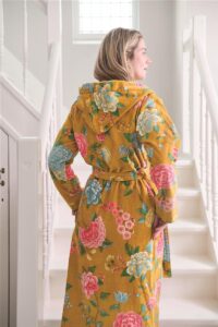 Een vrouw draagt de Pip Studio Good Evening-badjas in geel, maat XL, een gele badjas met roze en blauwe bloemen en een ceintuur.