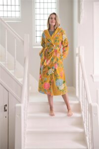 Een persoon staat op blote voeten op witte traptreden en draagt de Pip Studio Good Evening-badjas in geel, maat XL, een gele badjas met bloemenprint, capuchon en zakken.