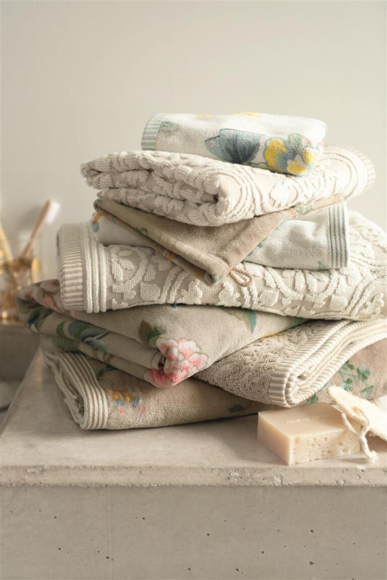 Een stapel stijlvolle, kleurrijke handdoeken van Pip Studio Good Evening Gastendoek Wit ligt op een steen naast een stuk zeep.