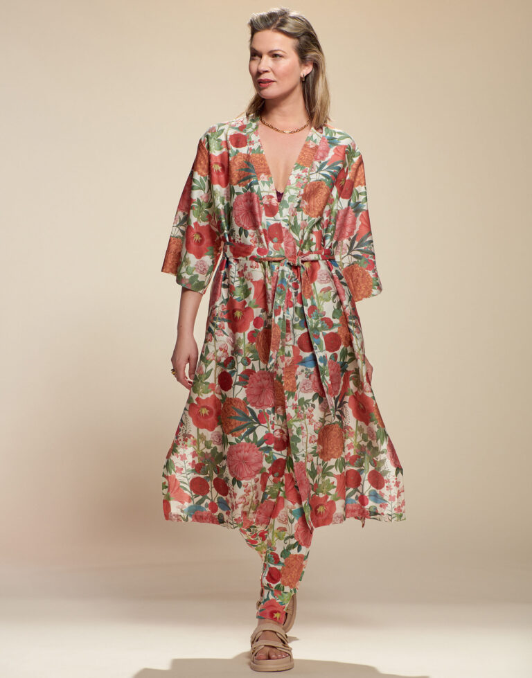 Een vrouw draagt de Essenza Ilona Florentien Kimono in Lobster Pink, gecombineerd met een bijpassende broek en sandalen, en glimlacht subtiel.