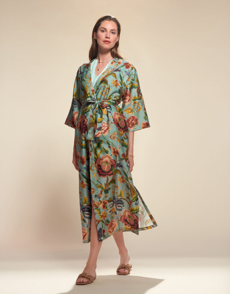 Een vrouw met lang haar en neutrale make-up draagt de Essenza Juliet Roselina Kimono in surfgroen, elegant vastgeknoopt in de taille en gecombineerd met platte sandalen.