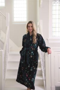 Een vrouw met lang blond haar glimlacht zacht terwijl ze de donkerblauwe Pip Studio Les Fleurs-badjas (XS) draagt.