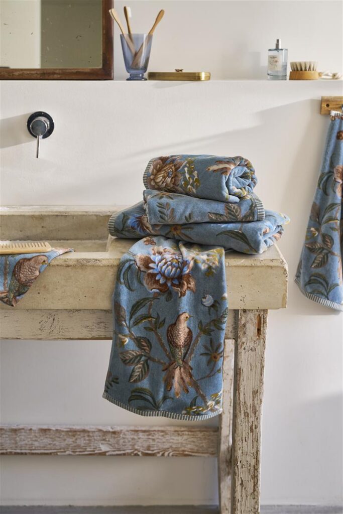 Op een rustieke wastafel ligt een stapel Pip Studio Secret Garden Washand Blauw-set van drie, met een bijpassende handdoek ernaast.
