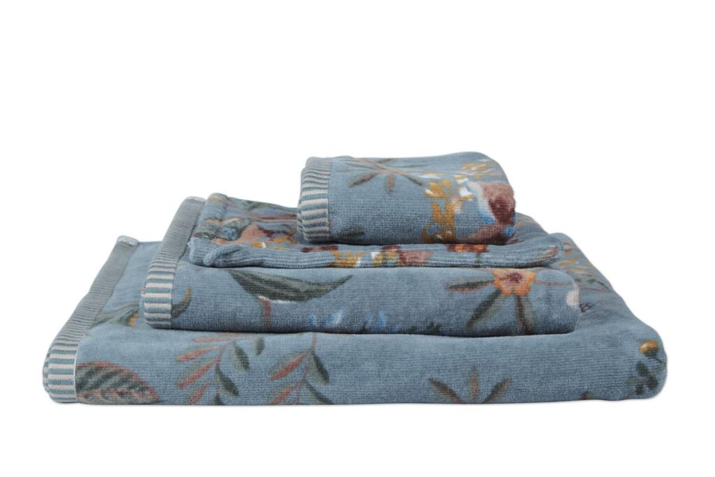 De handdoeken uit de Pip Studio Secret Garden Washand Blauw-serie zijn voorzien van een kleurrijk bloemenpatroon en gestreepte randen, en netjes opgestapeld van groot naar klein.