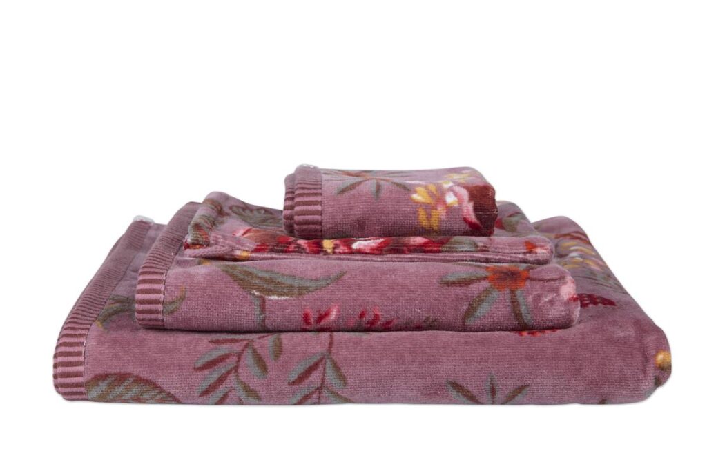 Drie opgevouwen mauve Pip Studio Secret Garden-washandjes en lichtpaarse handdoeken met bloemenpatroon liggen netjes opgestapeld.