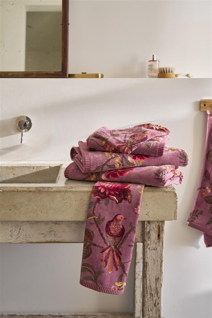 Op een rustieke badkamerwastafel liggen de lila Pip Studio Secret Garden-handdoekjes met bloemen en vogels netjes opgestapeld.