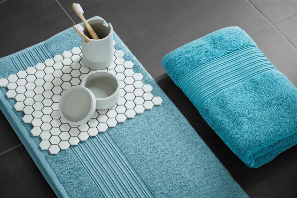 De Beddinghouse Sheer Gastendoek Blauw-set ligt op donkere tegels, met daarop een beker met tandenborstel en decoratieve accessoires.
