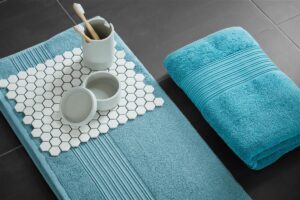 De Beddinghouse Sheer Gastendoek Blauw-set ligt op donkere tegels, met daarop een beker met tandenborstel en decoratieve accessoires.