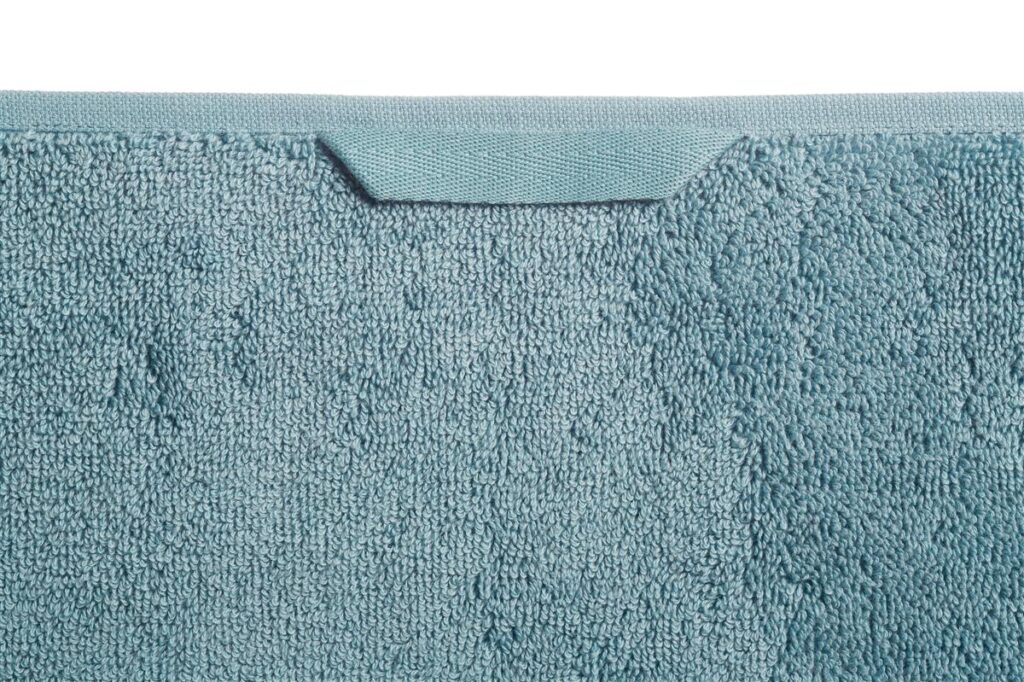 Close-up van het Beddinghouse Sheer gastendoek in blauw met een lichtblauwe structuur en een rechthoekig label aan de bovenrand.