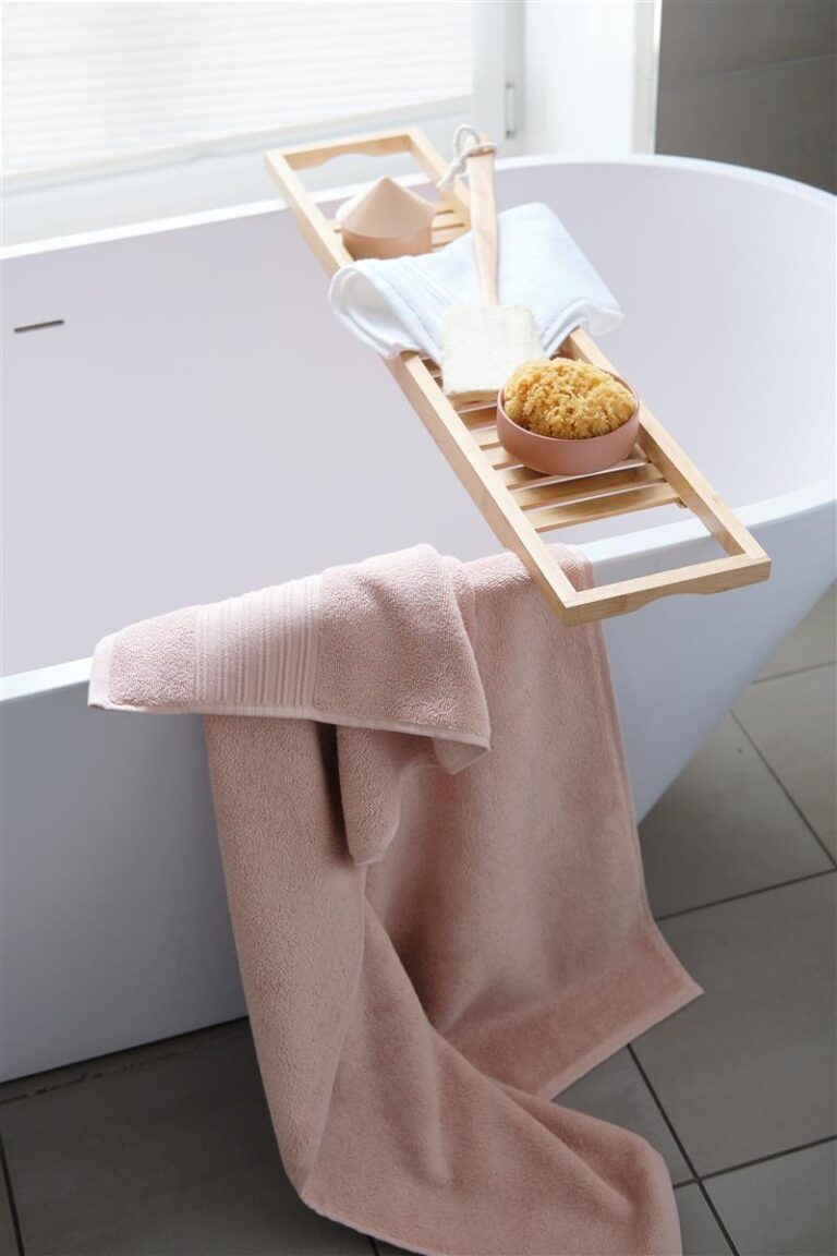 Op een houten dienblad op de badrand liggen een spons, zeep, een washandje en een handdoek; een Beddinghouse Sheer-badhanddoek in zachtroze hangt over de rand.