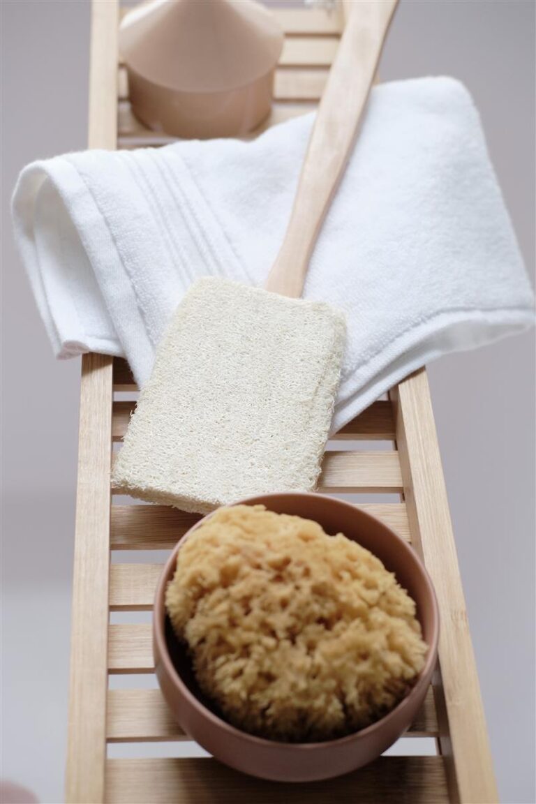 Op de houten badplank liggen een opgevouwen Beddinghouse Sheer Washand Wit-set, een badborstel met spons, een ronde natuurspons in een schaaltje en een beige zeepbakje.
