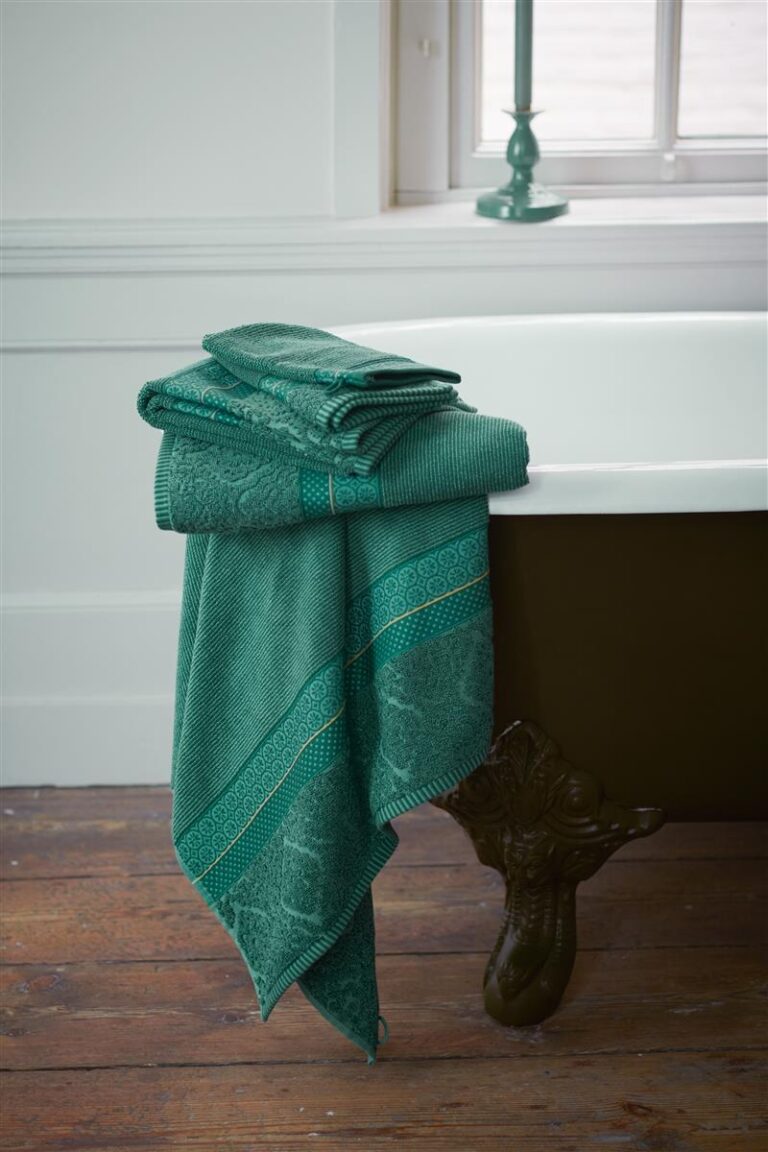 In een lichte badkamer met houten vloer ligt een stapel Pip Studio Soft Zellige gastendoekjes in groen op de rand van het bad.