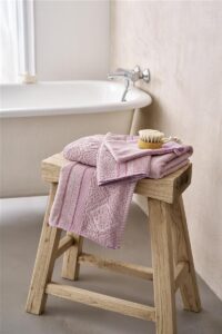 Op een houten kruk liggen opgevouwen roze handdoeken van Pip Studio Soft Zellige Gastendoek Lila naast een badborstel bij het vrijstaande bad.