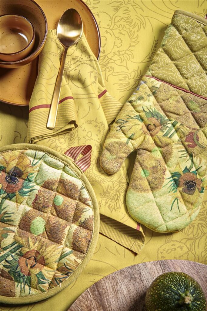 In een zonnige keuken liggen de Van Gogh Sunflower ovenwant (geel) met bijpassende pannenlap, gele borden en limoen op een bloemetjeskleed.