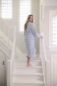 Een lachende vrouw draagt de Pip Studio Tile de Pip-badjas in blauw (maat S) en staat op blote voeten op een trap in een lichte ruimte.