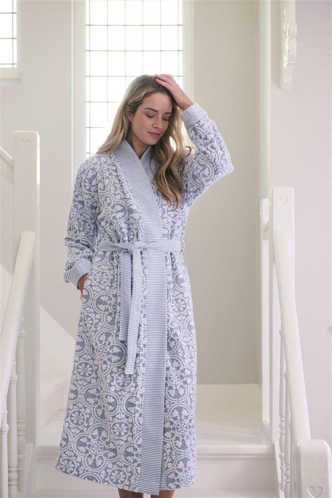 Een vrouw draagt de Pip Studio Tile de Pip-badjas in maat S; het blauw-witte patroon komt prachtig tot zijn recht in het zachte daglicht.