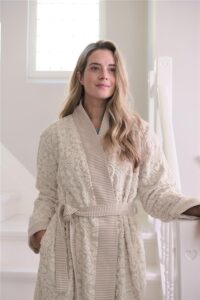 Een vrouw met lang, golvend blond haar draagt de Pip Studio Tile de Pip-badjas in de kleur Khaki M, met structuur en een ceintuur, verlicht door zacht licht.