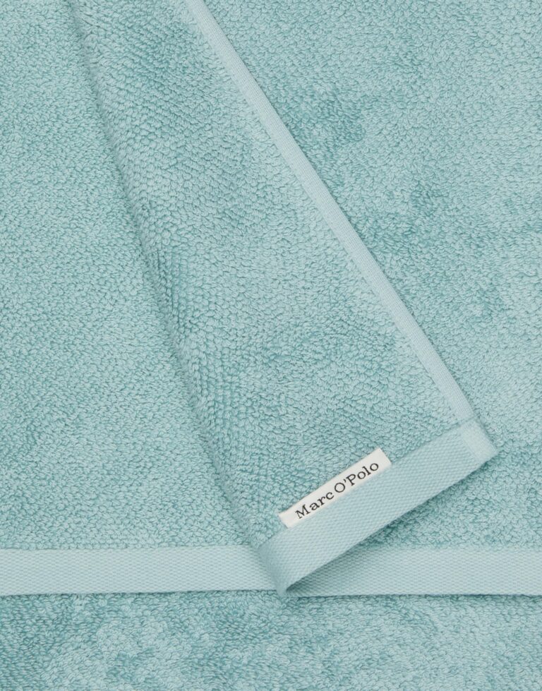 Deze close-up van de Marc O'Polo Timeless gastendoek in de kleur Aquamarine laat de rijke structuur, de nette afwerking en het merklabel zien.