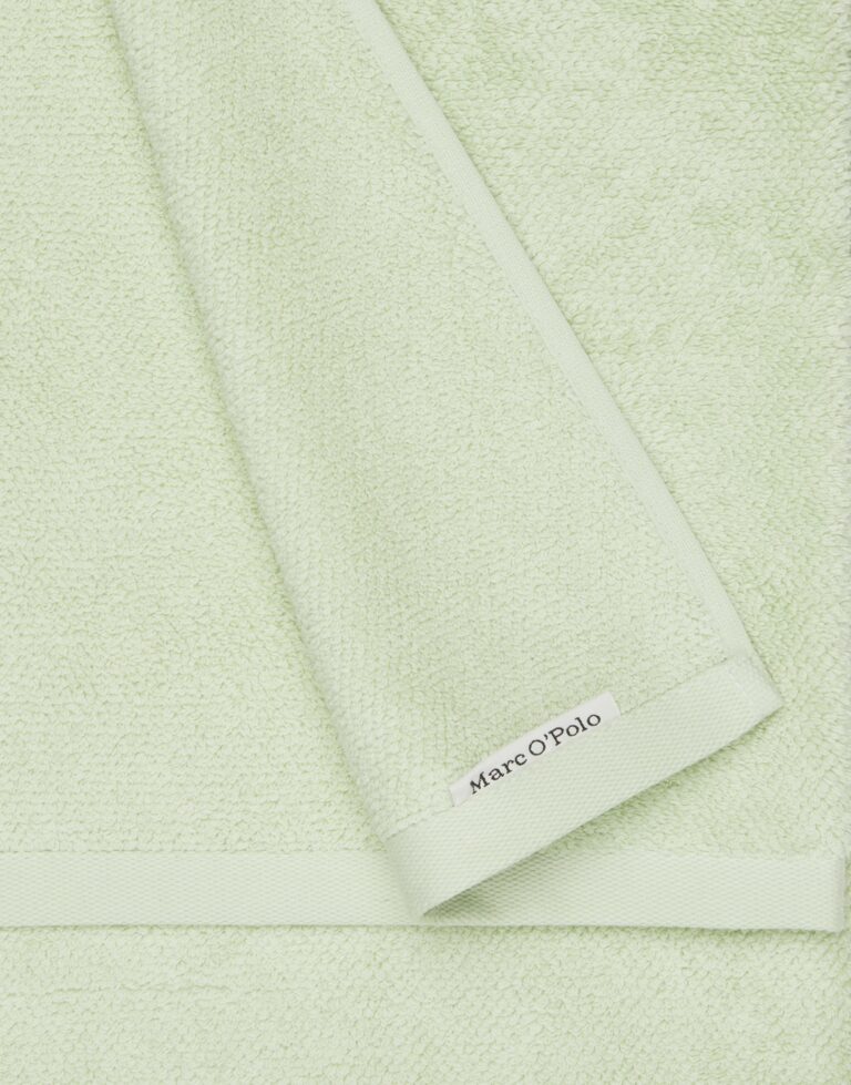 Het lichtgroene Marc O'Polo Timeless gastendoek is van dichtbij te zien met een zichtbare structuur, een omgeslagen hoek en een wit label met het merk langs de rand.