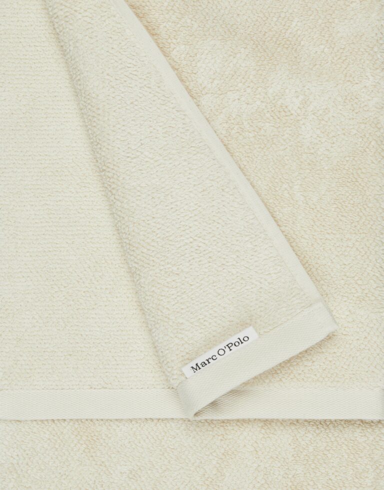 De Marc O'Polo Timeless Gastendoek Oatmeal is een netjes gevouwen, crèmekleurige handdoek met een subtiel gestikt label.