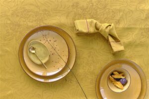 Een geel gedekte tafel met borden met patroon, een schaaltje gedroogd fruit, een gouden lepel en een servet op het Van Gogh Tournesol tafelkleed Yellow.