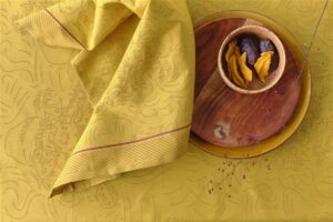 Het Van Gogh Tournesol-tafelkleed, geel met patroon en een roodgestreepte rand, ligt over de tafel met een houten schaal en rode bessen.
