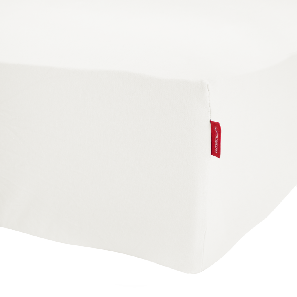 Een close-up van het Beddelicious Premium Jersey-hoeslaken in de kleur Ivory op een matras, met een rood stoffen label in de hoek.