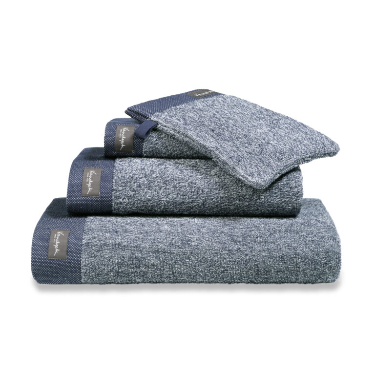 De Vandyck Home Mouline Badlaken Blue ink is een netjes gevouwen blauwgrijze handdoek met donkerblauwe randen en een label.