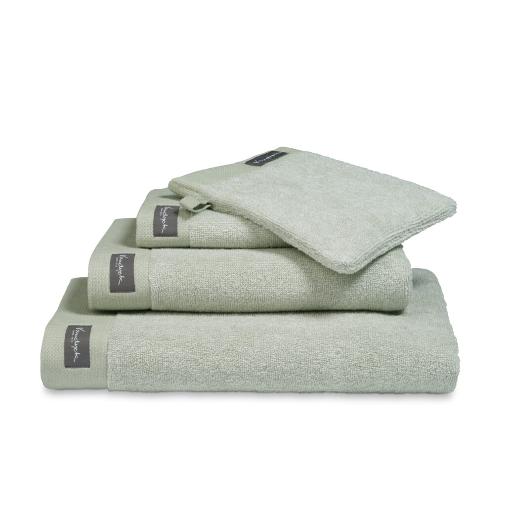 De Vandyck Home Mouline-badhanddoek in rookgroen met een grijs label is netjes opgevouwen en straalt luxe uit.