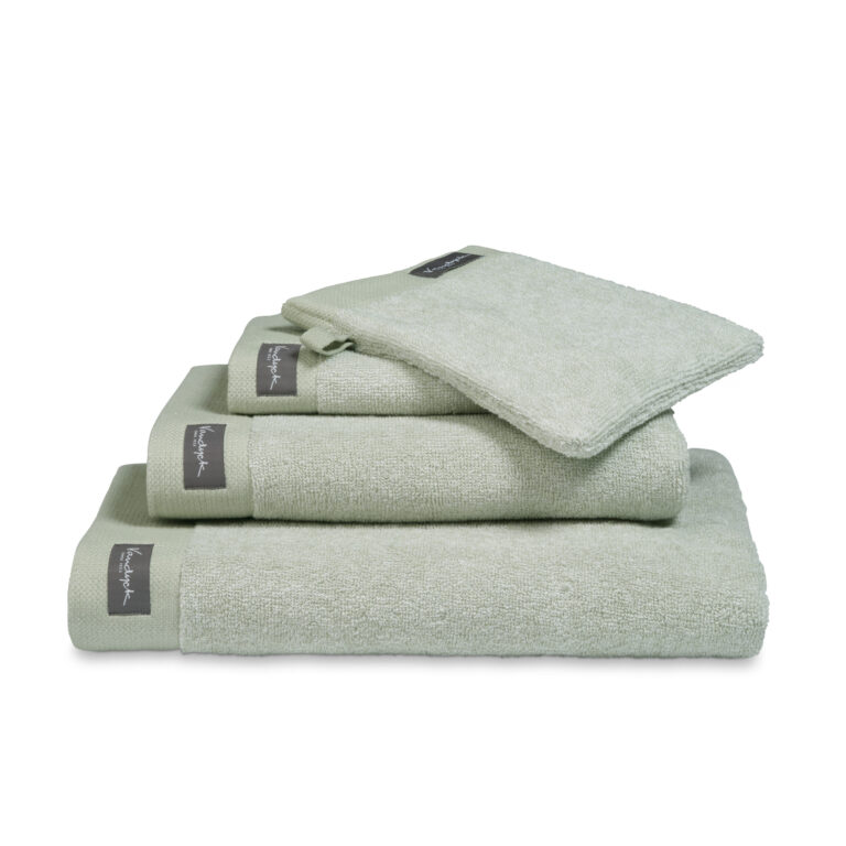 De Vandyck Home Mouline-badhanddoek in rookgroen met een grijs label is netjes opgevouwen en straalt luxe uit.