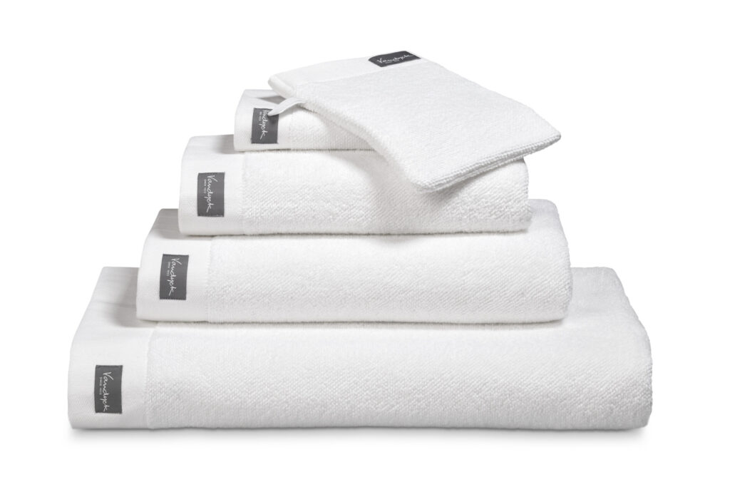 De Vandyck Home Uni Badlaken White-handdoeken liggen netjes opgestapeld, elk voorzien van een grijs label, met daarbovenop een washandje.