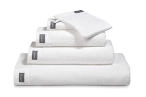 De Vandyck Home Uni Badlaken White-handdoeken liggen netjes opgestapeld, elk voorzien van een grijs label, met daarbovenop een washandje.