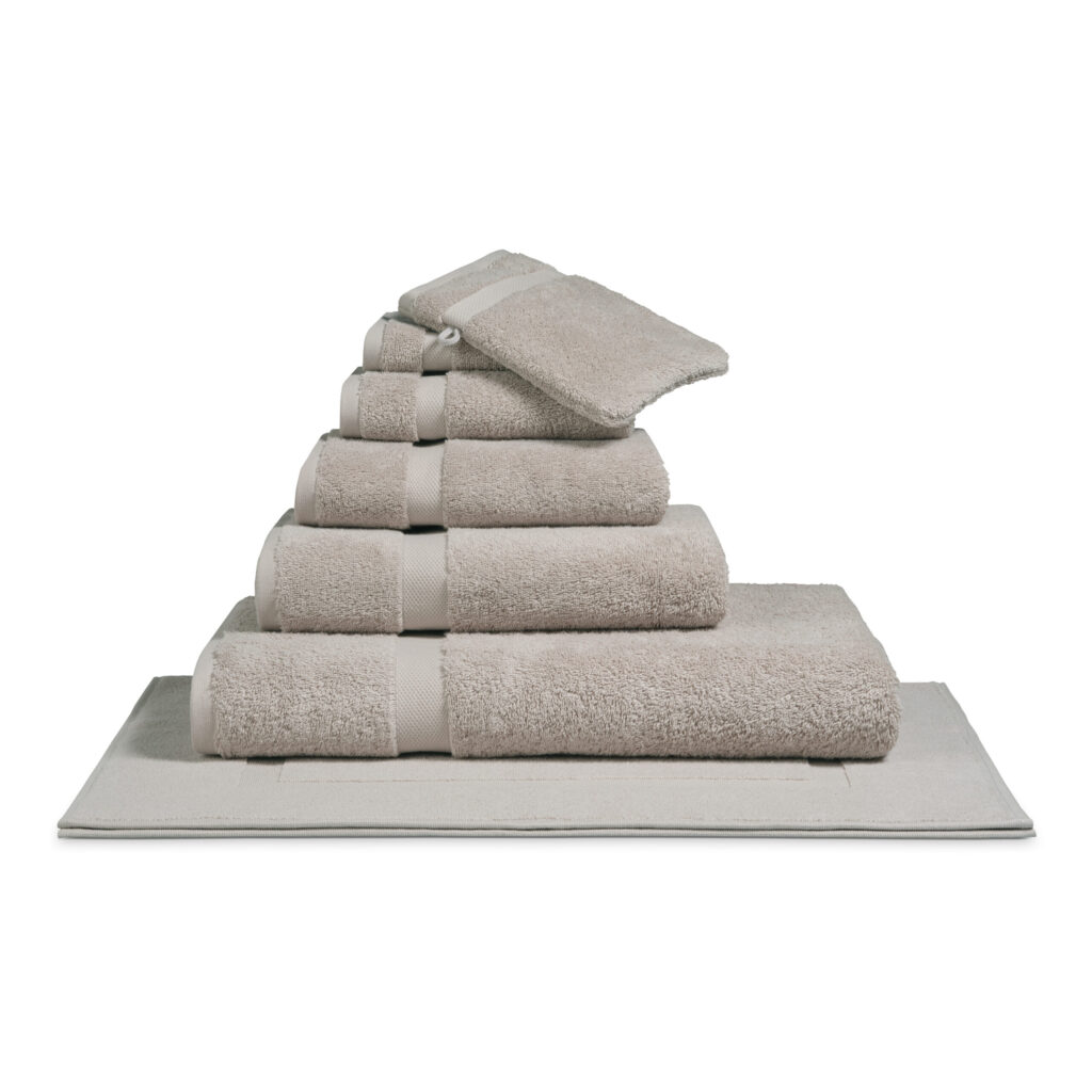 Het De Vandyck Ranger Badlaken Stone-badhanddoek ligt netjes opgevouwen en laat zijn elegante beige kleur en hoogwaardige afwerking goed tot hun recht komen.