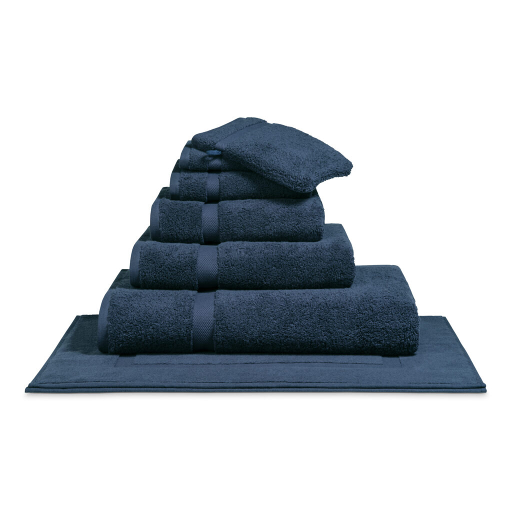 De Vandyck Ranger-badlakens in blauw zijn netjes opgestapeld, samen met blauwe handdoeken in verschillende maten en een badmat eronder.