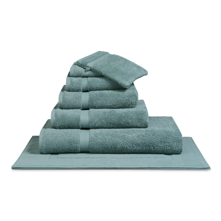 Het De Vandyck Ranger-badlaken in de kleur Mineral Blue ligt netjes opgevouwen op een bijpassende badmat en wordt stijlvol gepresenteerd.