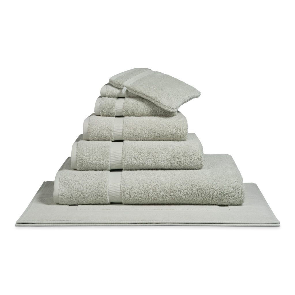 Het Vandyck Ranger-badlaken in de kleur Pale Olive ligt netjes opgevouwen in een stapel op een bijpassende badmat.