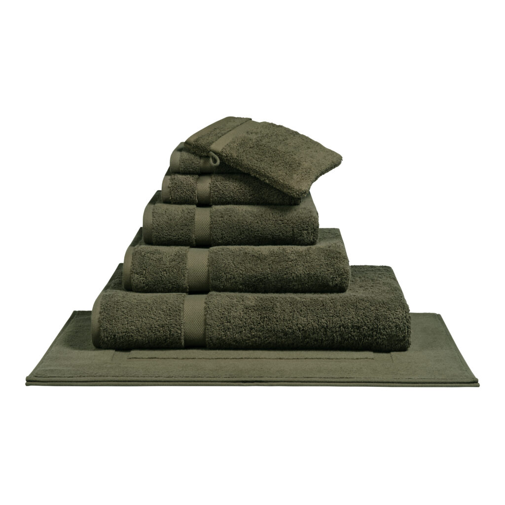 Het De Vandyck Ranger-badlaken in de kleur Thyme ligt netjes opgevouwen, samen met bijpassende handdoeken en washandjes, in een piramide op de badmat.