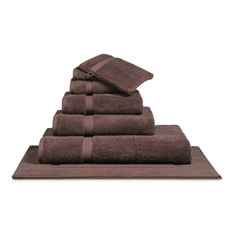 Het Vandyck Ranger-badlaken in Rose taupe ligt netjes opgevouwen op een bijpassende badmat en zorgt zo voor een rustige uitstraling.