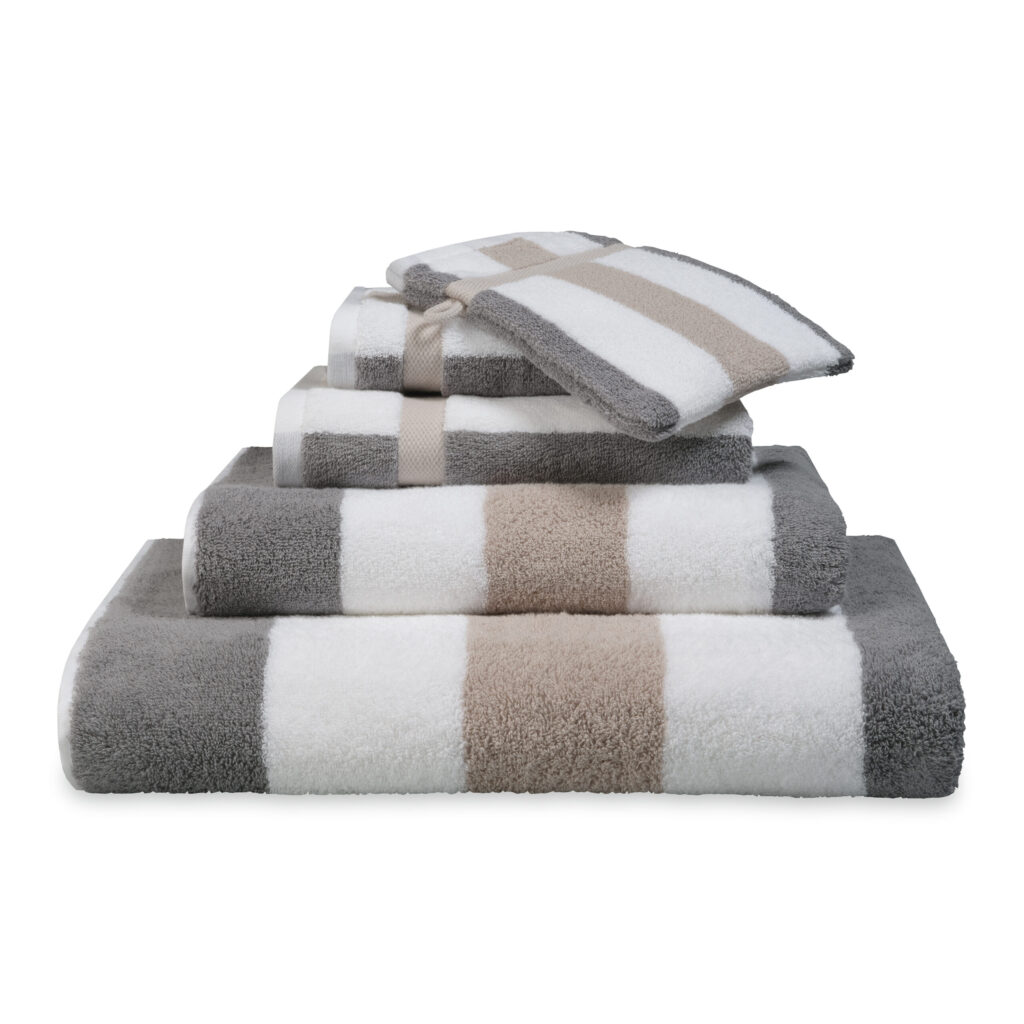 De Vandyck Vancouver Badlaken Stone heeft brede horizontale strepen in wit, beige en grijs, met bijpassende washandjes erbij.