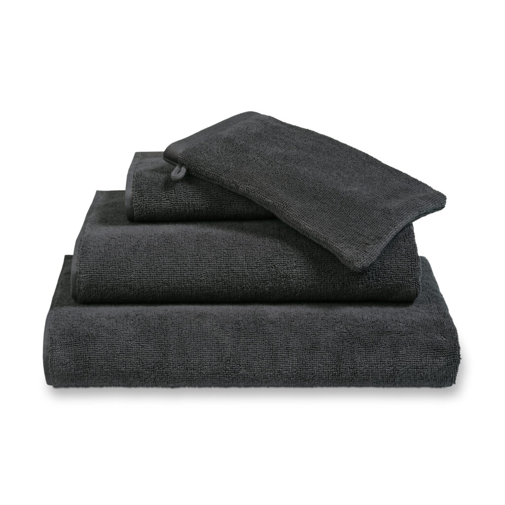 Een keurig gestapelde Vandyck Verona Plain badlaken-set in Off Black, bestaande uit een groot badlaken, een washandje en een handdoek.