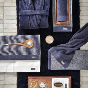 Een flatlay met het Vandyck Home Petit Ligne-badlaken Blue Ink, gecombineerd met een marineblauwe badjas, een kaars en verzorgingsproducten.