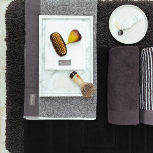 Een stijlvolle badkamer met handdoeken uit de Vandyck Home Petit Ligne-collectie in de kleur Off Black, grijze accenten en accessoires op een marmeren dienblad.