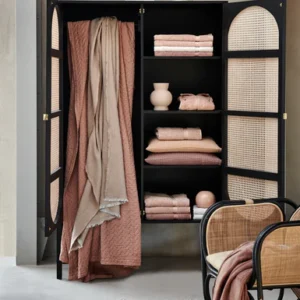 In een modern, minimalistisch interieur staan op een zwarte rotankast nette Vandyck Ranger Badlaken Praline-handdoeken en keramiek uitgestald.
