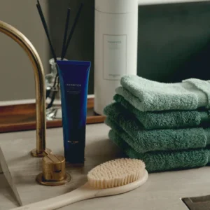 Op het badkamermeubel liggen zachte Vandyck Ranger Handdoek Cream tan-handdoeken naast een houten borstel en verzorgingsproducten.