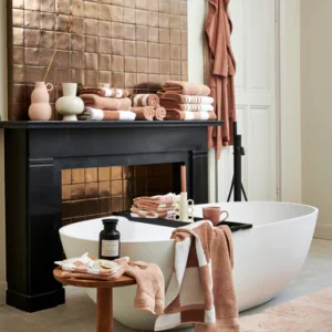 Een moderne badkamer met een ovaal bad, vazen en decoraties op een zwarte rand. Op het krukje liggen zeep en de Vandyck Ranger Handdoek Praline.