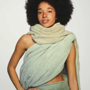 Een persoon met krullend haar en sproeten poseert vol zelfvertrouwen, gehuld in de Vandyck Ranger-handdoek in de kleur Smoke green.
