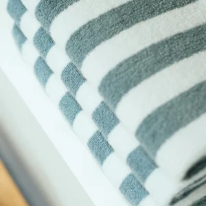 Het De Vandyck Verona Stripes-badlaken in parelblauw is netjes opgevouwen en heeft een patroon van afwisselende witte en blauwe strepen.
